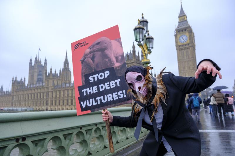 Person dressed as a debt vulture outside Big Ben and Parliament, holding a placard which says Stop the Debt Vultures