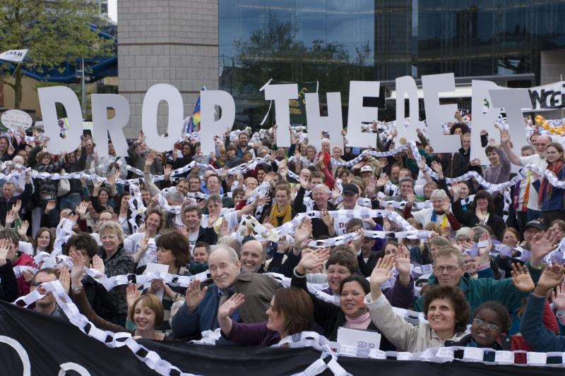 Crowd holding paper chains and letters spelling Drop the Debt